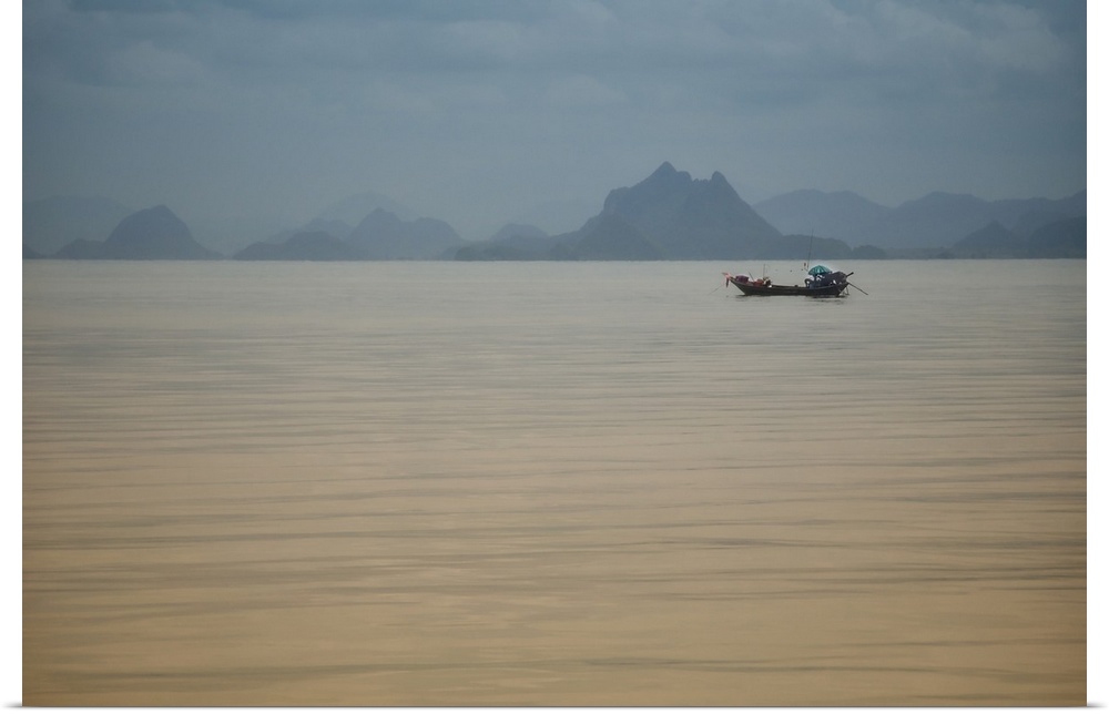 Single fishing boat in Thailand sea in the area of the Kho Phi Phi islands with mountains away, a blue and grey mood.