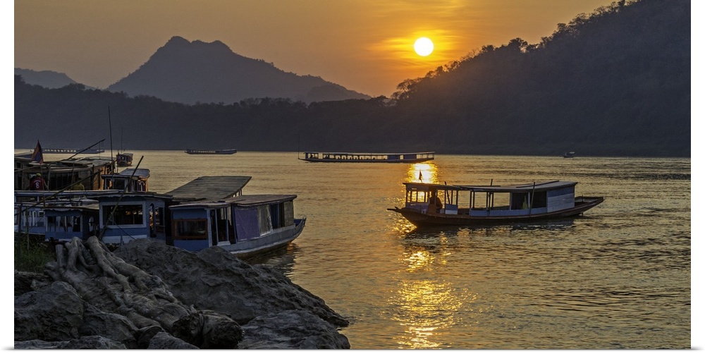 The sun low in the sky over fishing boats on the river in a valley in Laos.