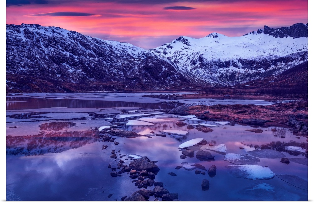 Snowy mountains in Lofoten, Norway, by a glacial lake at sunset.
