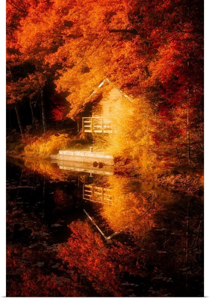 A small house at the edge of the water with deep orange leaves surrounding it.
