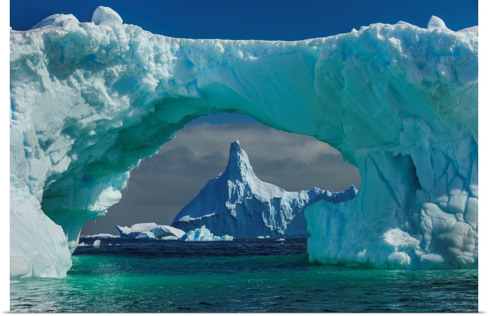 The peak of an Antarctic mountain seen through the natural arch of a turquoise glacier.