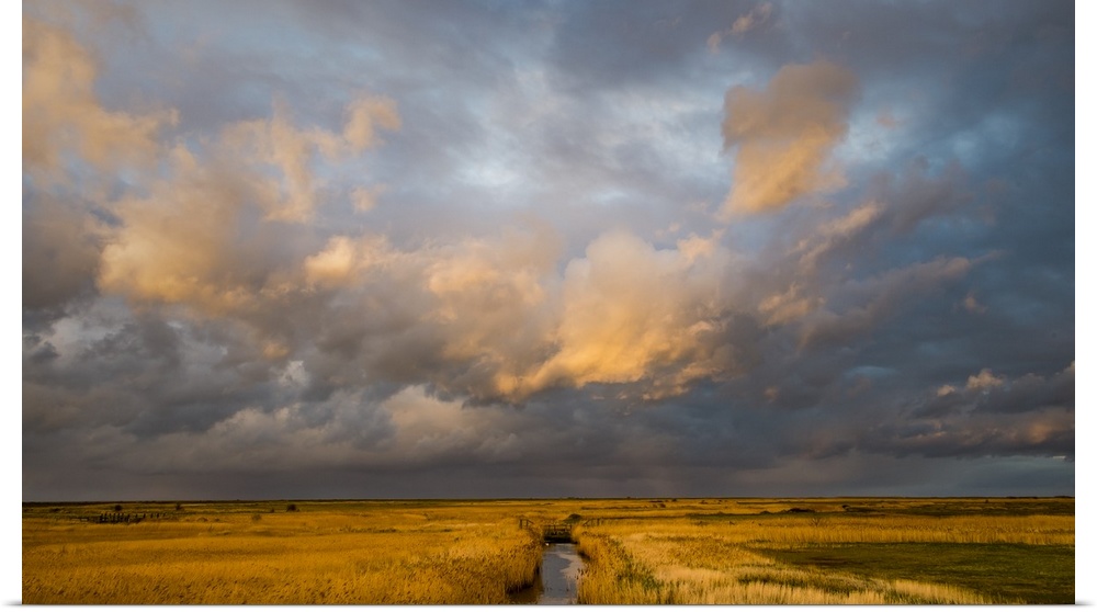 Photograph of a beautiful skyscape in Norfolk, England, with a stream in the center moving towards the horizon line and li...