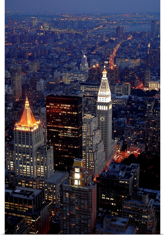 This vertical artwork is an aerial photograph of a Manhattan skyscrapers illuminated in the evening.
