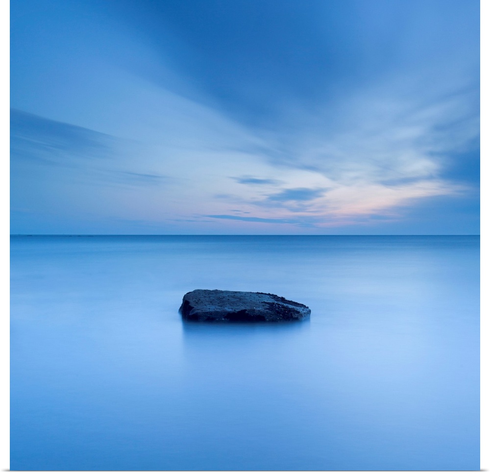 A zen calm minimal minimalist cool deep blue image of one rock in a flat calm sea.