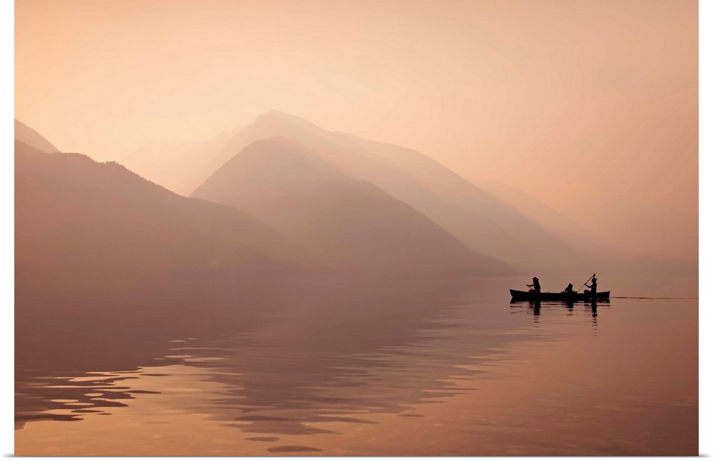 A photograph of people in a rowboat on lake beside mountains in silhouette.