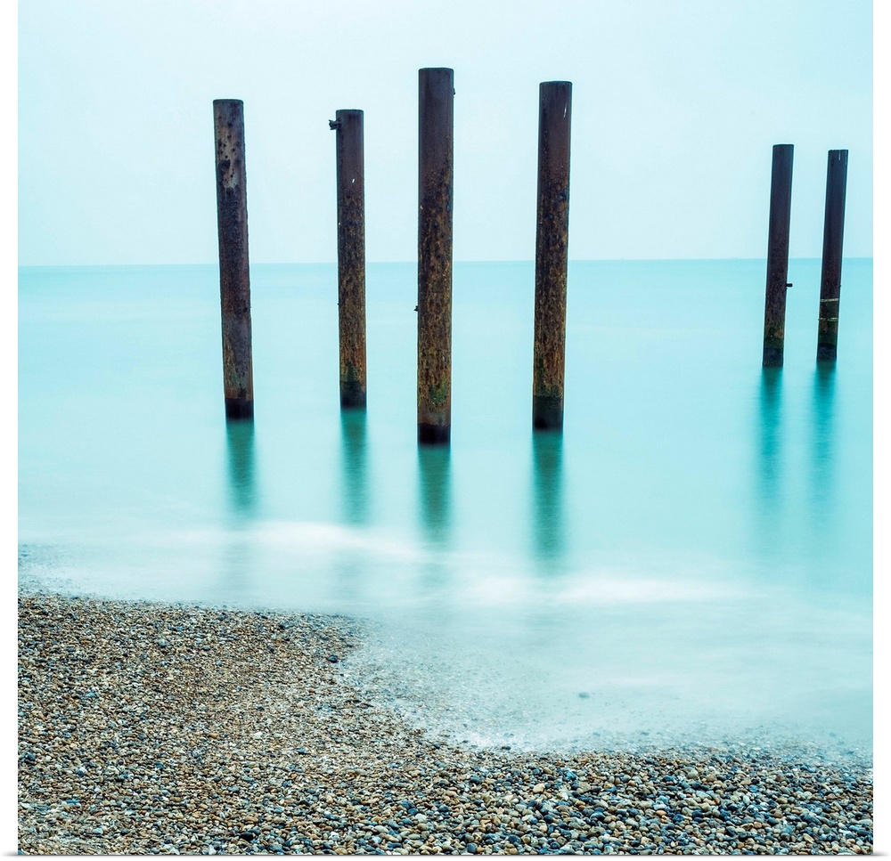 A photograph of wooden poles from a pier sticking up from the water along a beach.