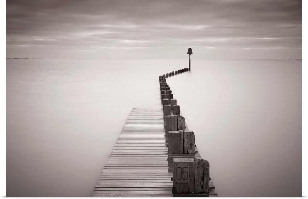 Photograph of dock stretching into ocean under a cloudy sky.