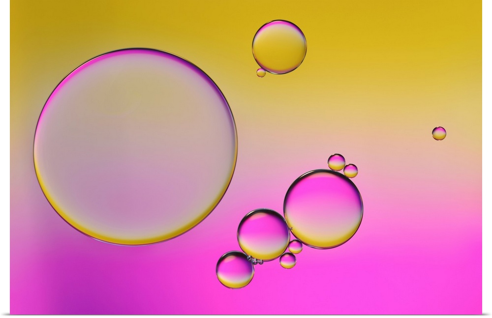 Closeup photograph of drops of oil in water with yellow and pink hues.