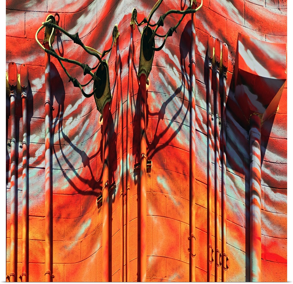 Conceptual photo of red and orange painted pipes and wires on the side of a building, warped to create an abstract image.