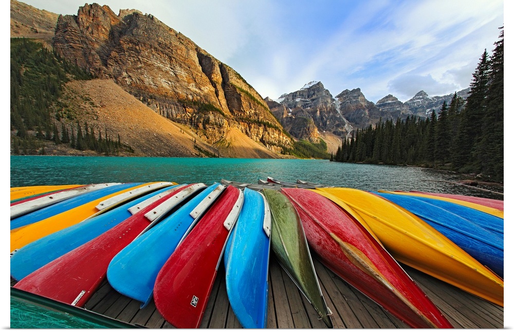 Large, horizontal photograph of colorful boats lined up on a dock at Moraine Lake.  The mountains in Banff National Park, ...