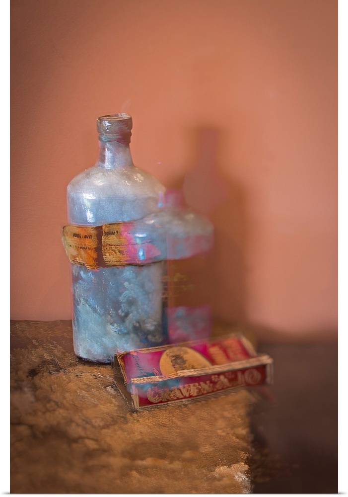 A distressed photo of a bottle and a box of cigarettes on textured table.
