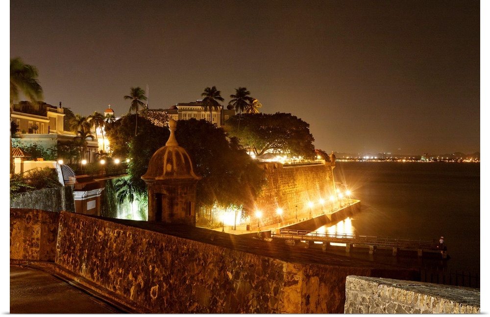Large photograph taken at nighttime focuses on a section of an illuminated shoreline within the capital city of Puerto Ric...