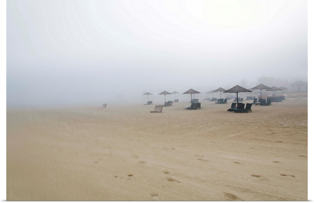 Landscape photograph of a sandy beach covered in fog and beach chairs with umbrellas.