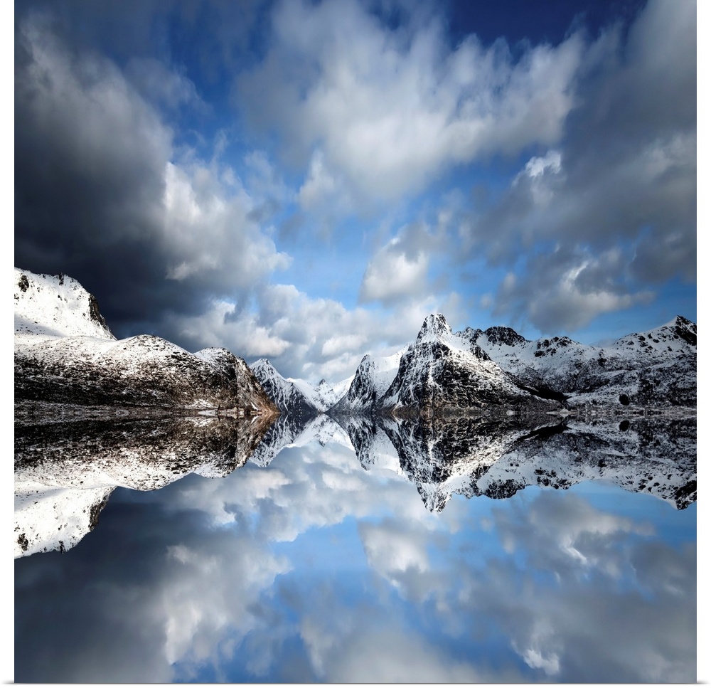 Photograph of a lake casting a mirror reflection of mountains and clouds.
