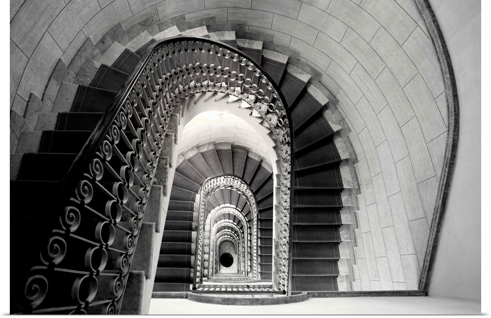 This architectural photograph looks down a historic stairwell lined with tile and iron work banister.
