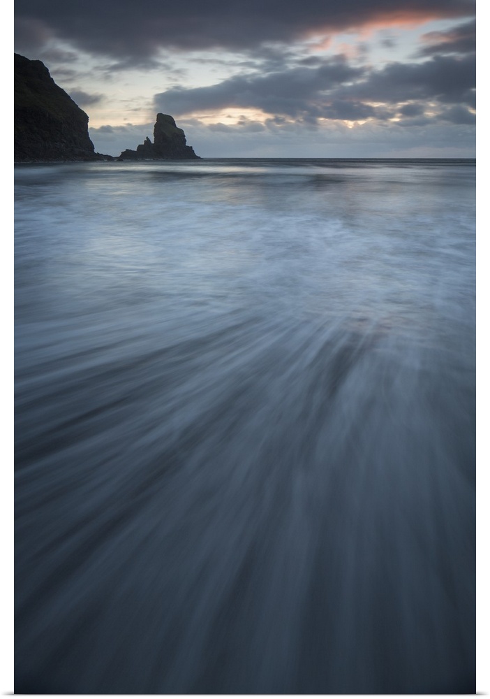 A dramatic sunset seascape from Talisker Bay, Isle of Skye, Scotland in soft blue greys and pinks with swooshing waves and...