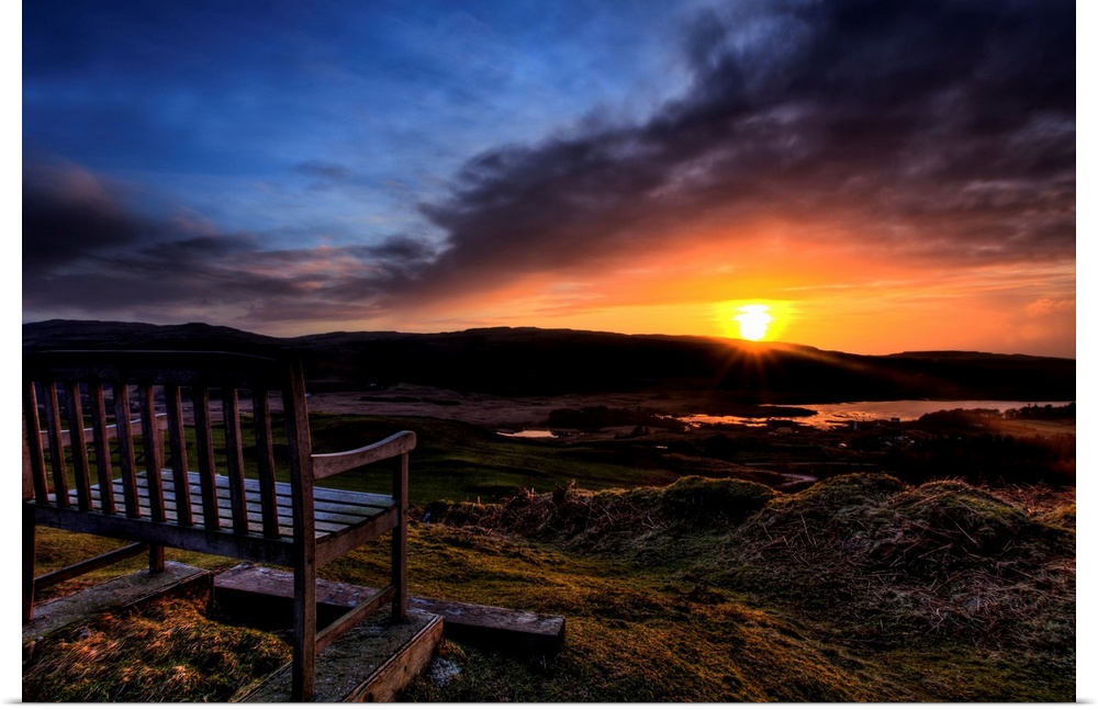 A wooden seat looking out over a Scottish view to a Loch with a golden sunset and dramatic sky.