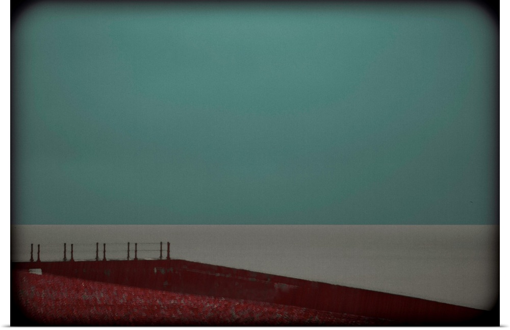 Minimalist photograph of a red landing leading up to a calm, gray sea with a turquoise sky and dark vignetted sides.