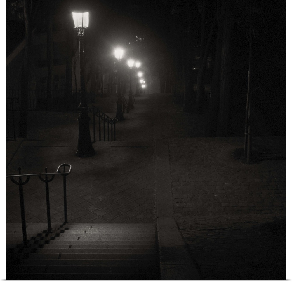 A timeless monochrome balck and white image of steps in Monmarte, Paris, France on a misty night with old iron street lamps.