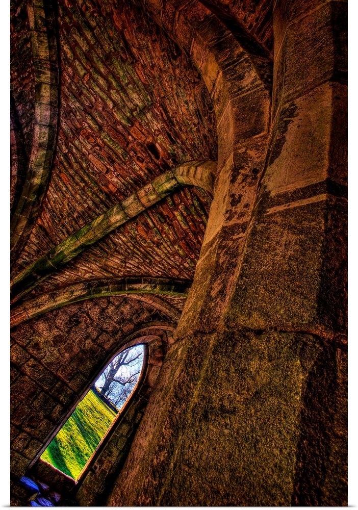 A dynamically angled gothic arched window beneath an ancient stone ceiling with views out to green fields and a winter tree.