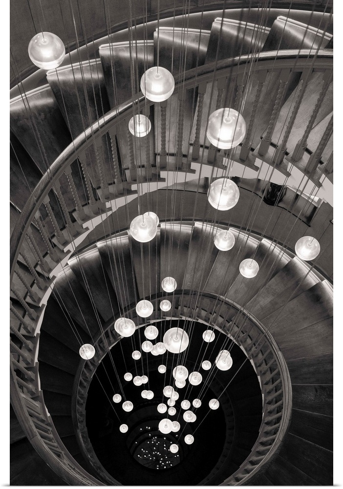 Fine art photo looking down a spiral staircase, with round lights in the center, in black and white.