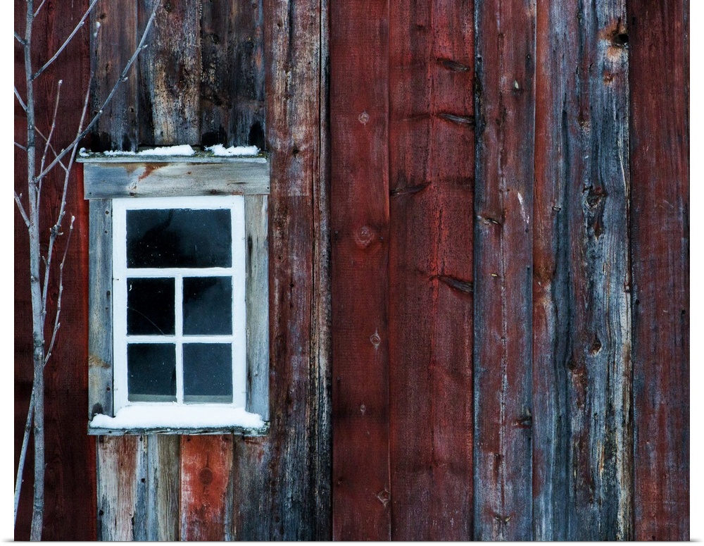 White window on the side of a weathered red barn.