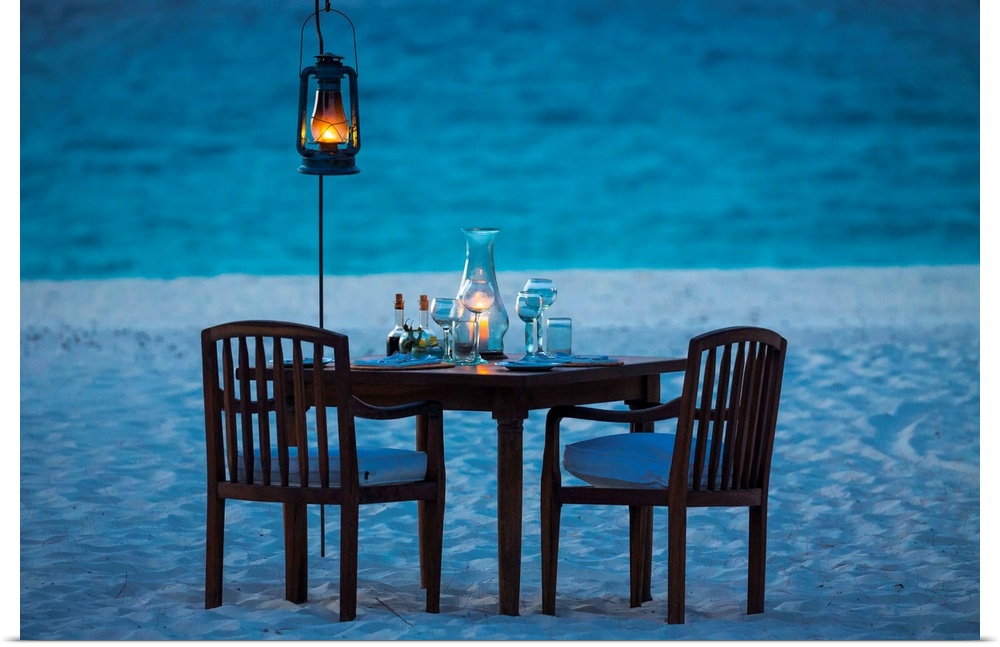 A photograph of a romantic table setting on a sandy beach at sunset.