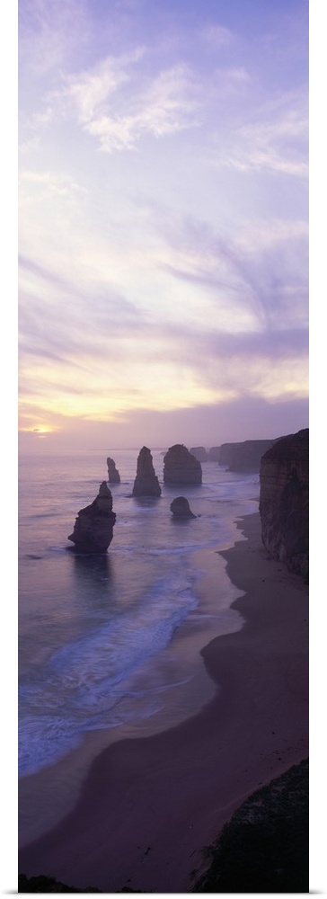 Vertical panoramic photograph of shore with tall vertical rock formations in the ocean under cloudy skies.