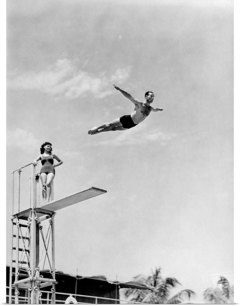 1930s 1940s Shapely Woman Watching Man Swan Dive Off High Diving Board.