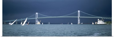 A storm approaches sailboats racing past Rose Island lighthouse and the Newport Bridge in Narragansett Bay, Newport, Rhode Island USA