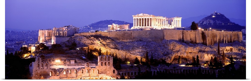 Panoramic image of Acropolis lit up at dusk as it sits high on a hill overlooking Athens, Greece.