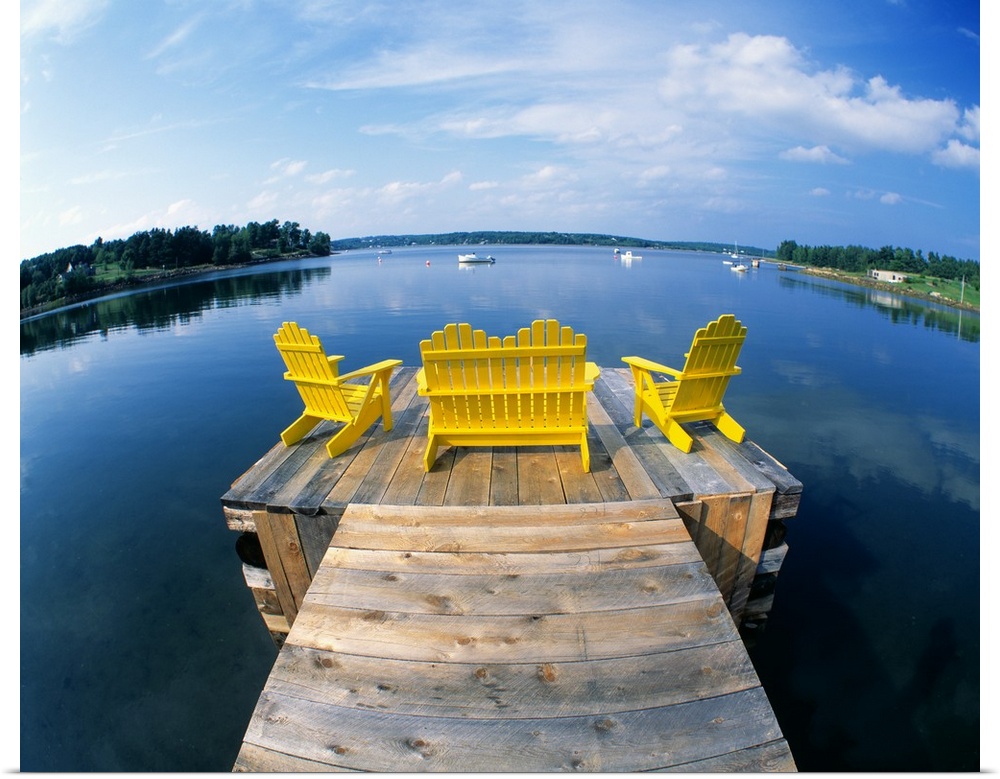 Outdoor wooden chairs sit at the end of a small dock and look out onto a large body of water.