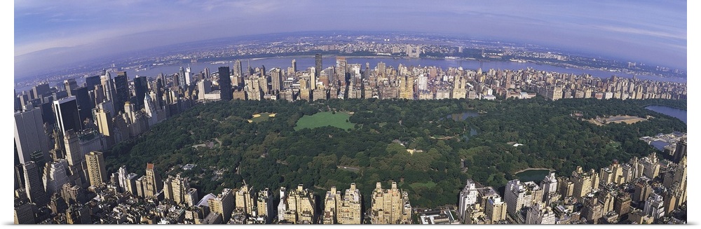 Wide angle, aerial photograph of Central Park beneath a blue sky, surrounded by the skyscrapers of New York City.