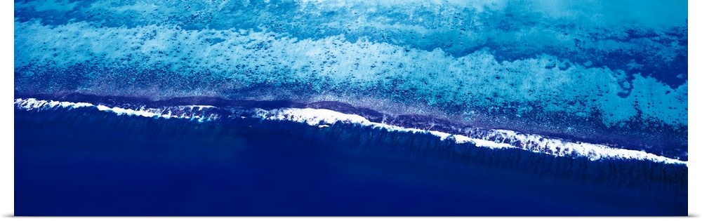 This is a panoramic photograph taken from above of waves breaking on the shore of this tropical reef.