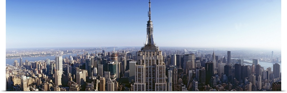 Wide angle, aerial photograph of New York City beneath a blue sky, the Empire State Building in the foreground.