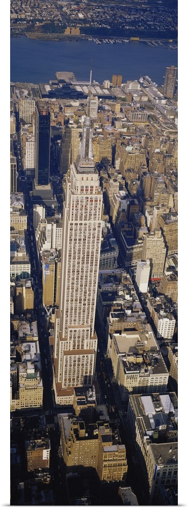 A long vertical picture taken from above the Empire State building which towers over the city surrounding it.