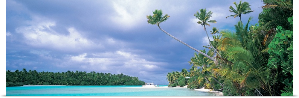 Panoramic photograph of lagoon with shoreline full of trees and tree covered island in distance under a cloudy sky.
