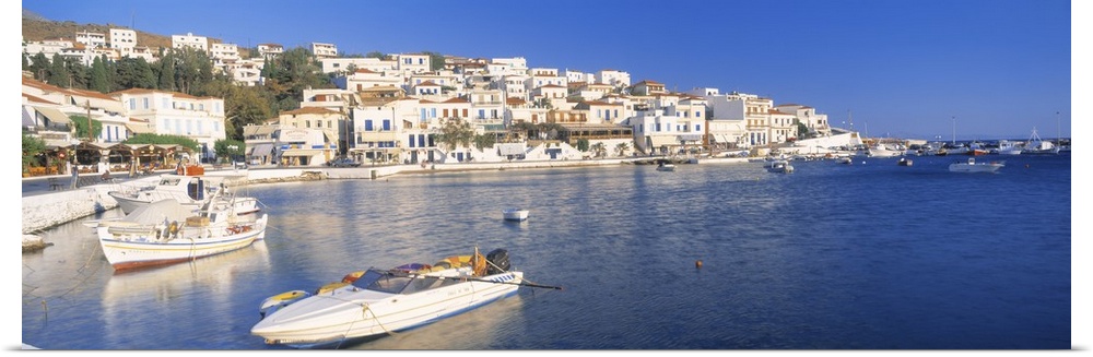 Houses in Greece are photographed from across the water where several boats sit docked.