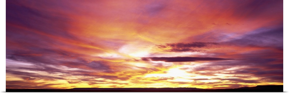 A panoramic photograph of clouds lit up in brilliant colors from the sun below the horizon.