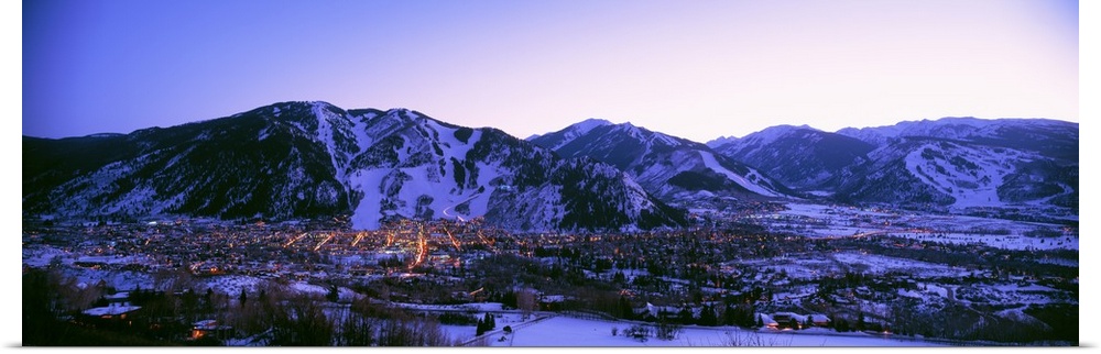 Long panoramic photo of Aspen Colorado at dust nestled in the valley of the snow covered mountains.