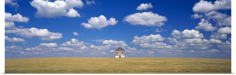 A single house is photographed from a distance as it sits on vast open land underneath a cloud filled sky.