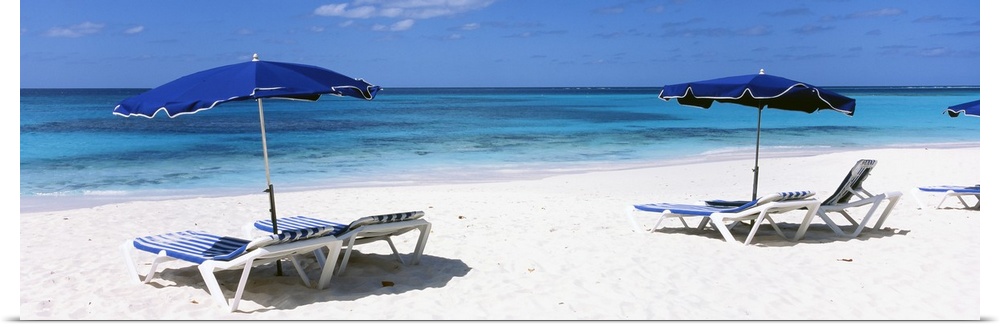 Beach chairs and umbrellas are pictured in panoramic view along the beach and close to the ocean.