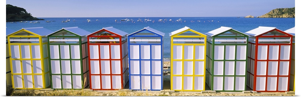 Panoramic photograph of colorful row of huts on the shoreline with the ocean in the distance.