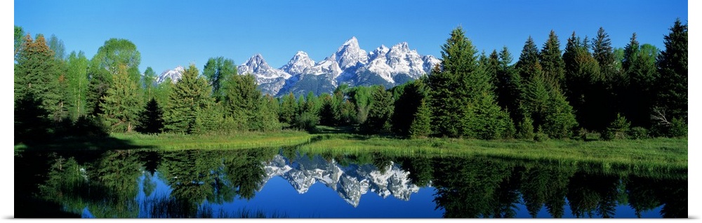 Pointed mountain peaks mirrored in the still waters of the lake below, surrounded by a dense forest of evergreen trees.