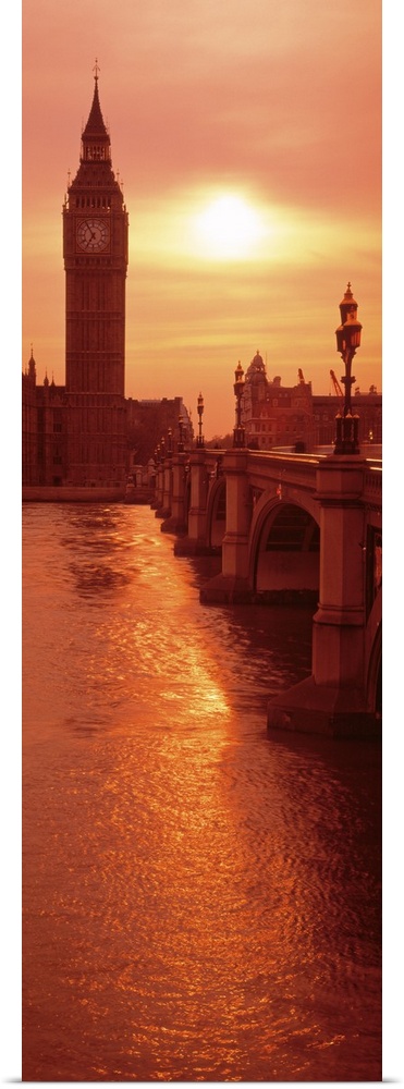 A vertical panoramic photograph taken of Big Ben from across the bridge and over a body of water. The sun is low in the sk...