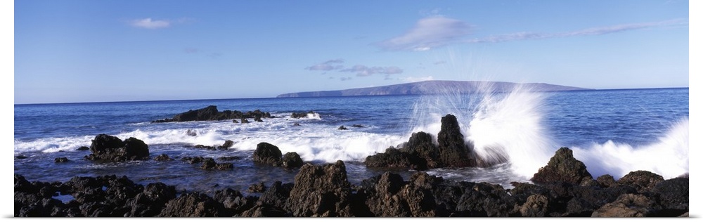 This panoramic photograph shows a wave breaking on the volcanic rock on the island shore.