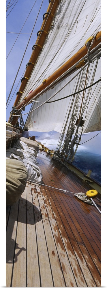 Vertical panorama of the deck of a sail boat as it tips starboard in water with the sails at full mast.