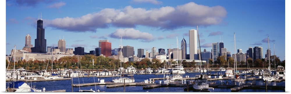 The Chicago skyline is a backdrop to a wide angle photograph taken of the harbor with several boats docked in the water.