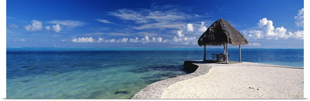 Panoramic view of a small straw hut sits on the beach that protrudes out into the clear blue ocean.