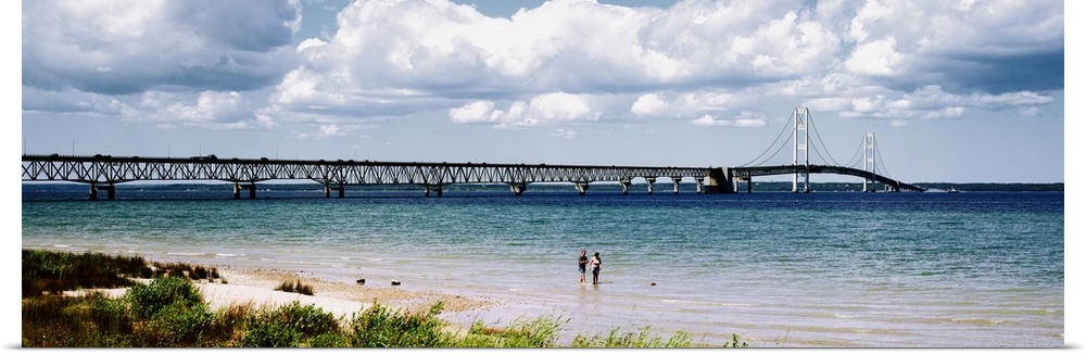 Panoramic picture of a massive bridge that stretches across a lake in Michigan. Some beach on the lake can be seen with tw...